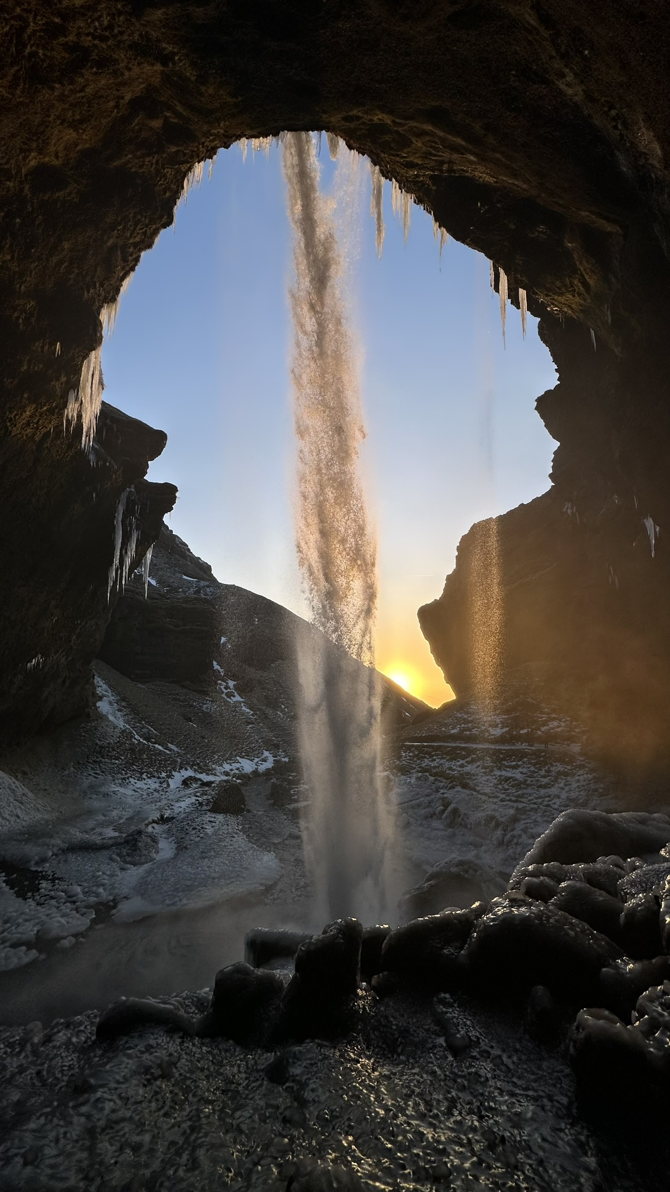 Cascata incorniciata dall'interno di una grotta scura con ghiaccioli