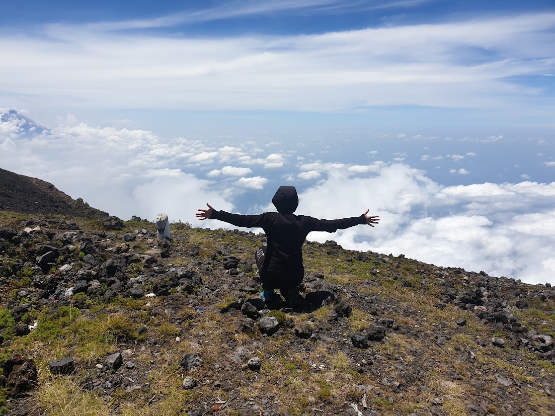 Escursionista a braccia aperte sulla cima del vulcano ammirando le nuvole dall'alto