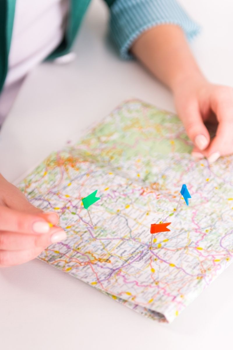 Mani che posizionano puntine su una mappa per travel design