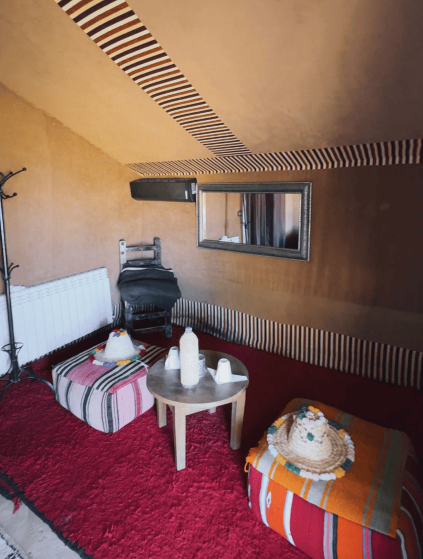 Interno spazioso della tenda con dettagli tipici, tavolino, pouf e tappeti rossi