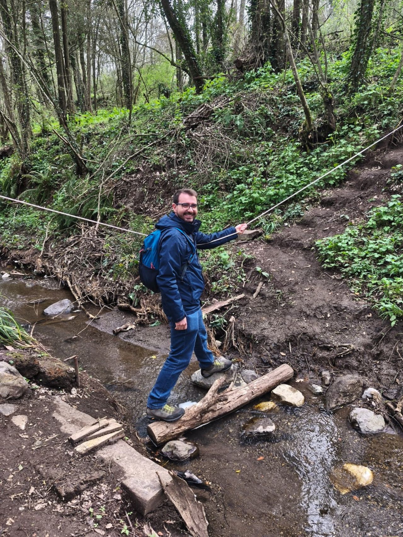 Escursionista sorridente sorreggendosi ad una fune mentre attraversa un torrente in equilibrio su un tronco