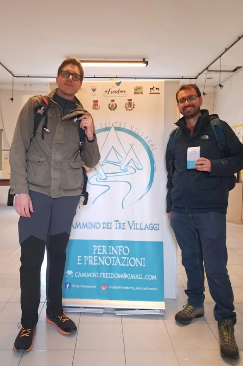 Due sorridenti camminatori posano orgogliosi accanto al banner informativo del Cammino dei Tre Villaggi