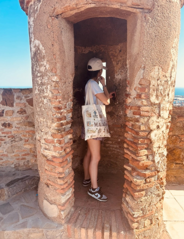 Emanuela Macciocca travel designer posa in una torretta difensiva in mattoni del Castillo de Gibralfaro a Málaga, guardando verso la costa