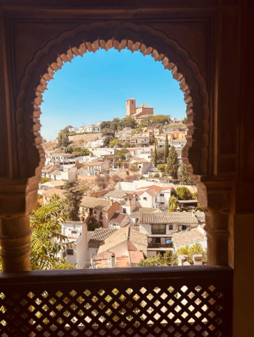 Emanuela Macciocca, travel designer, posa di profilo guardando fuori da un'ampia finestra ad arco finemente scolpita a Dar al-Horra a Granada, con vista sull'Alhambra e El Albacín