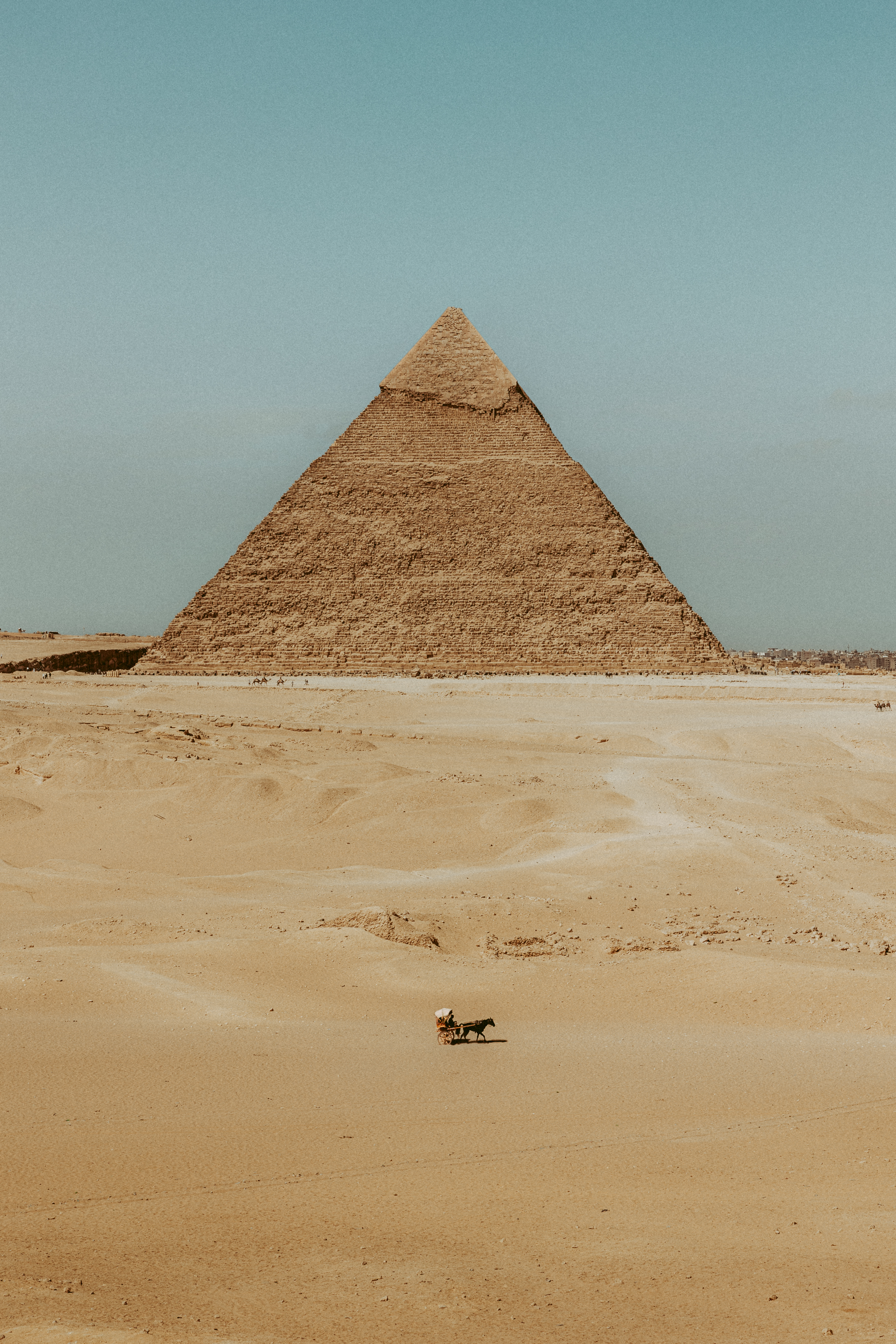La Grande Piramide di Giza si staglia contro il cielo azzurro, con una piccola carrozza nel deserto