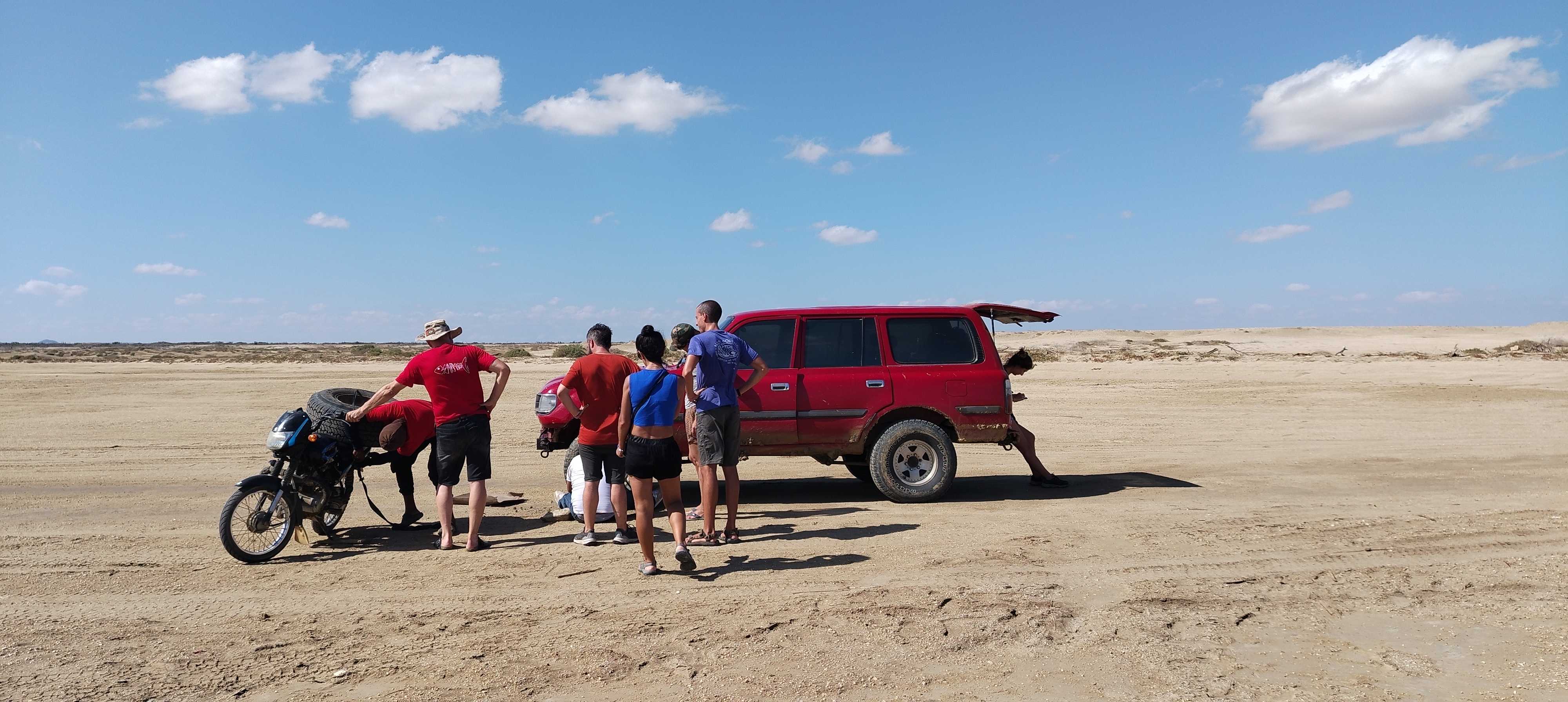 Gruppo di viaggiatori fermi intorno a un fuoristrada rosso nel mezzo del deserto arido