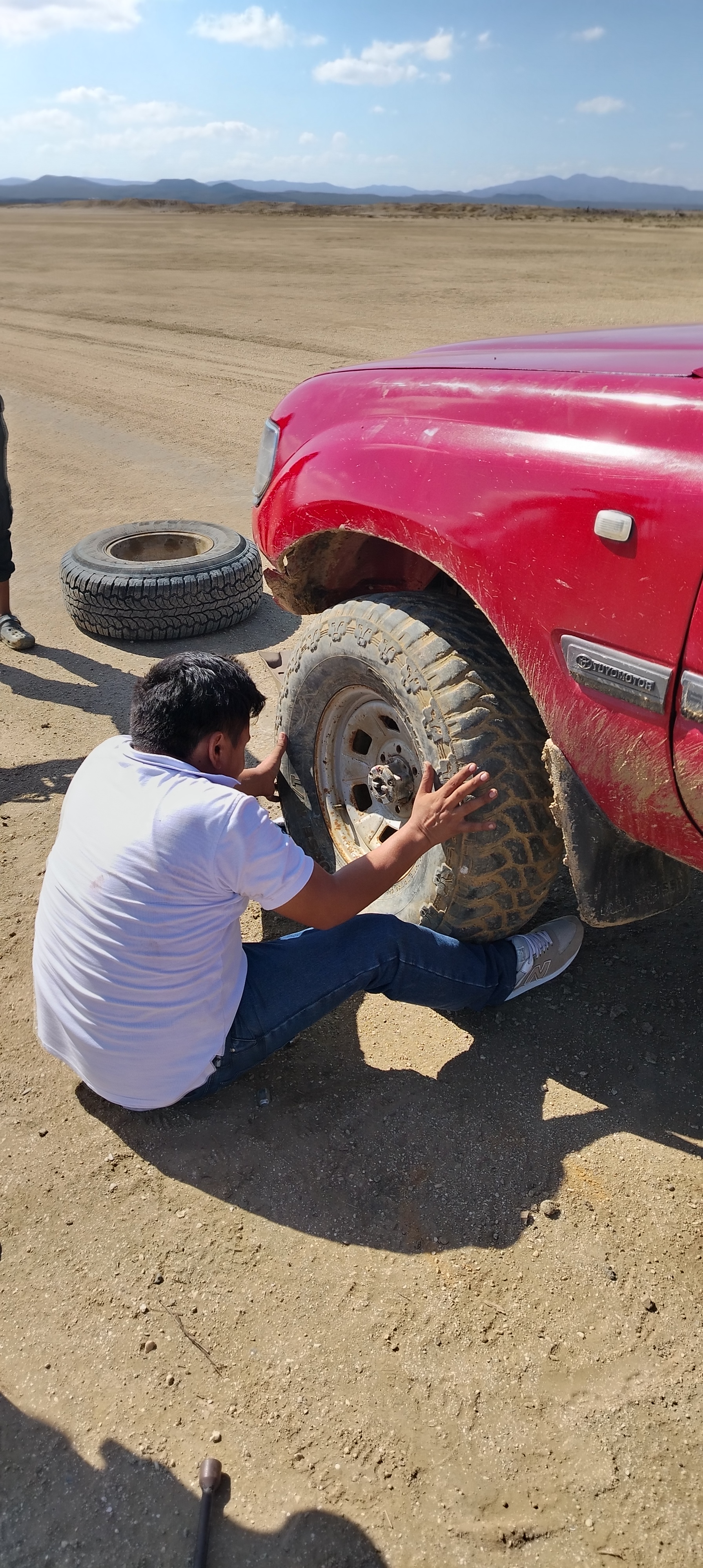 Ragazzo locale seduto a terra che sostituisce lo pneumatico bucato del veicolo