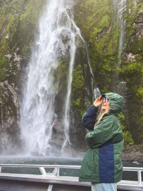 ragazza in primo che sorride e sullo sfondo una cascata in un viaggio in Nuova Zelanda